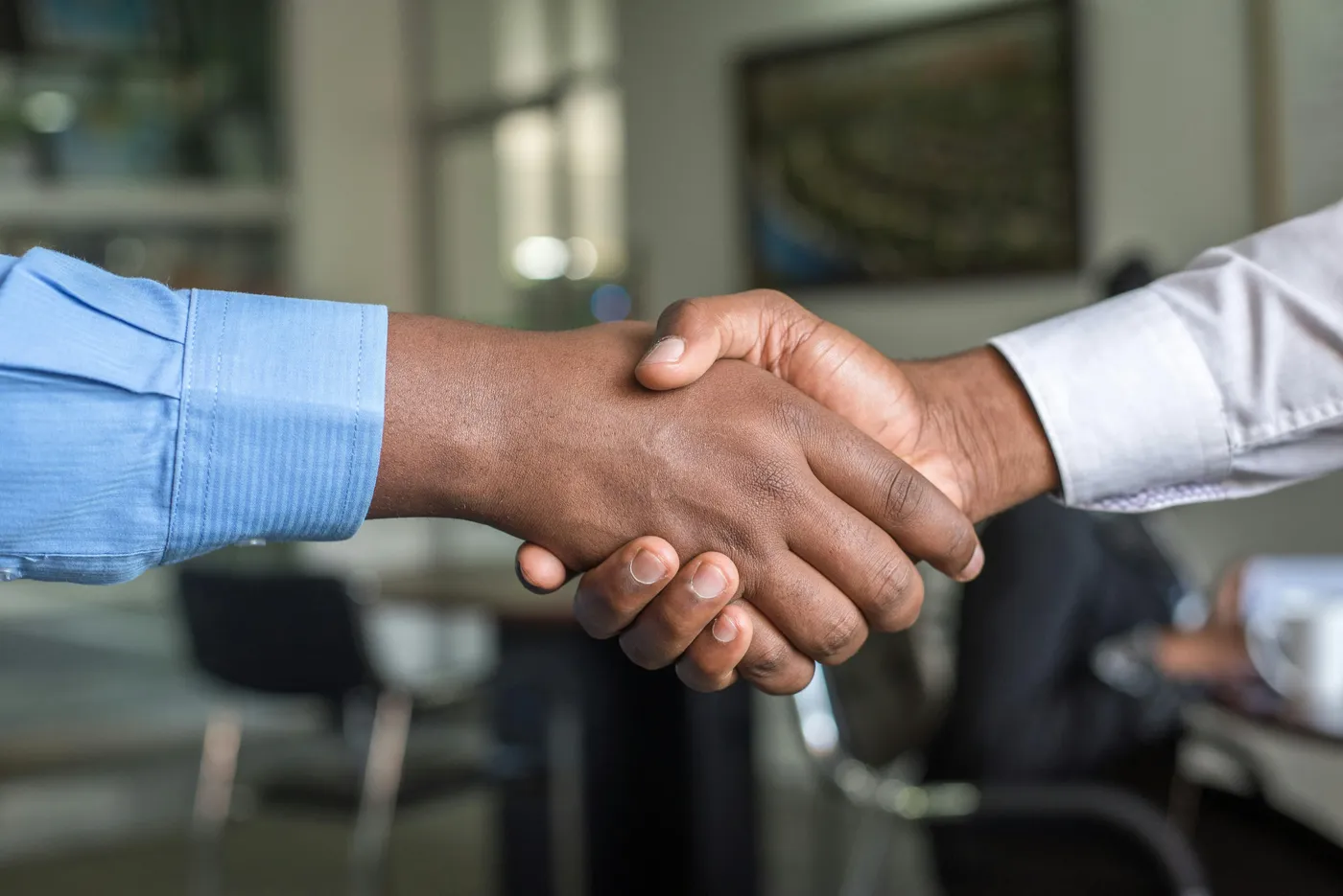 A close-up of a firm handshake between two people in business shirts, symbolizing an agreement in a professional office setting.