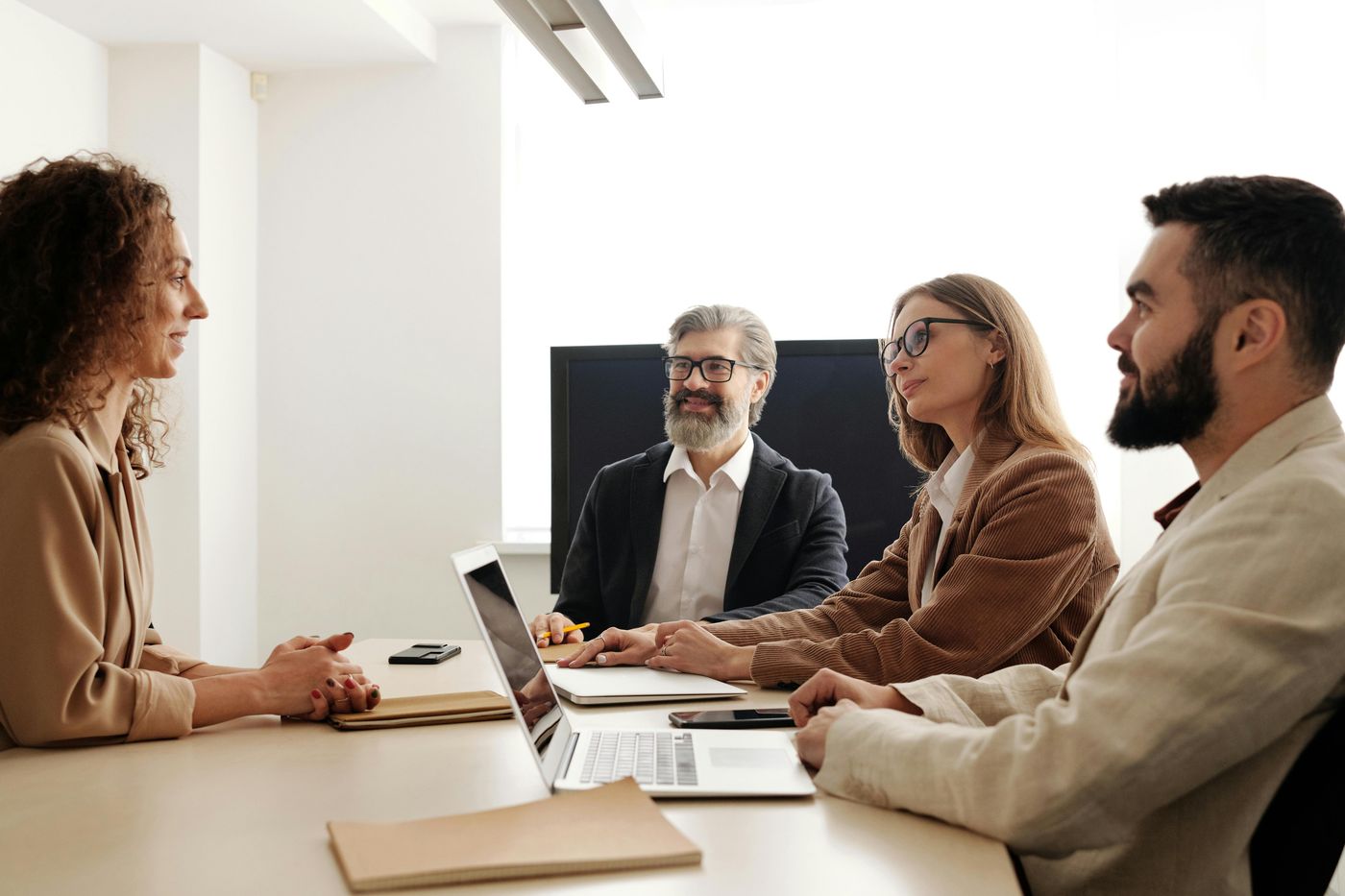 A woman speaks to three professionals seated across from her at a long conference table, who are listening attentively.