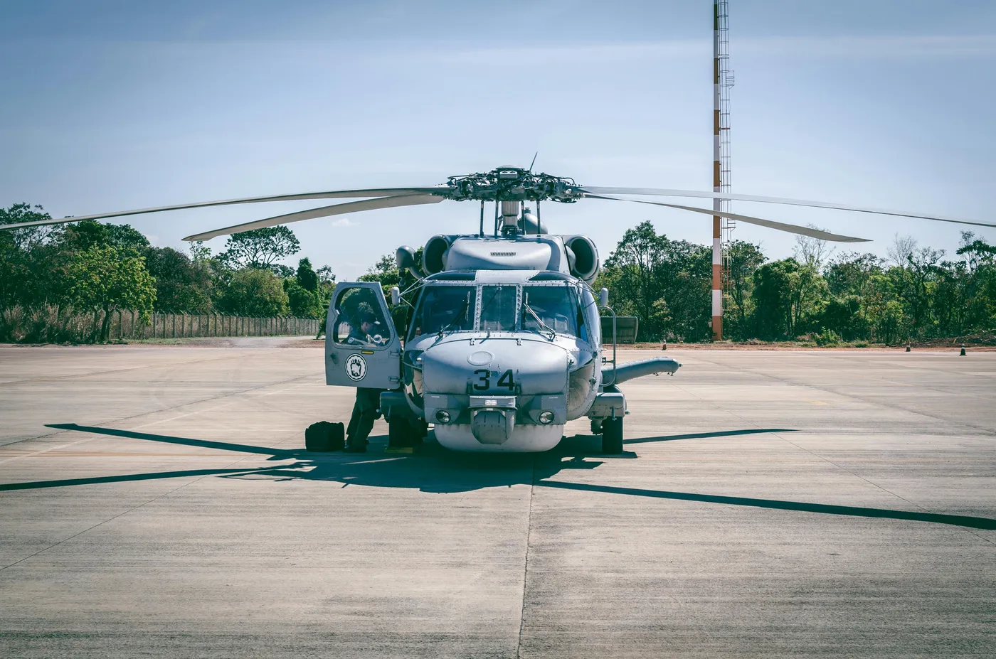 A front view of a gray helicopter parked on an airfield tarmac on a clear day, with its side door open.