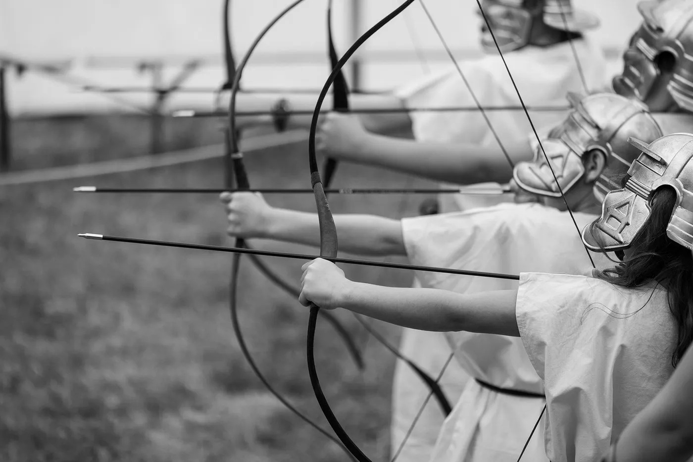 A row of archers in ancient warrior costumes drawing bows and arrows in unison