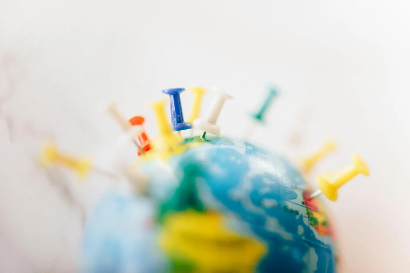 Colorful push pins stuck into a small desktop globe against a white background.