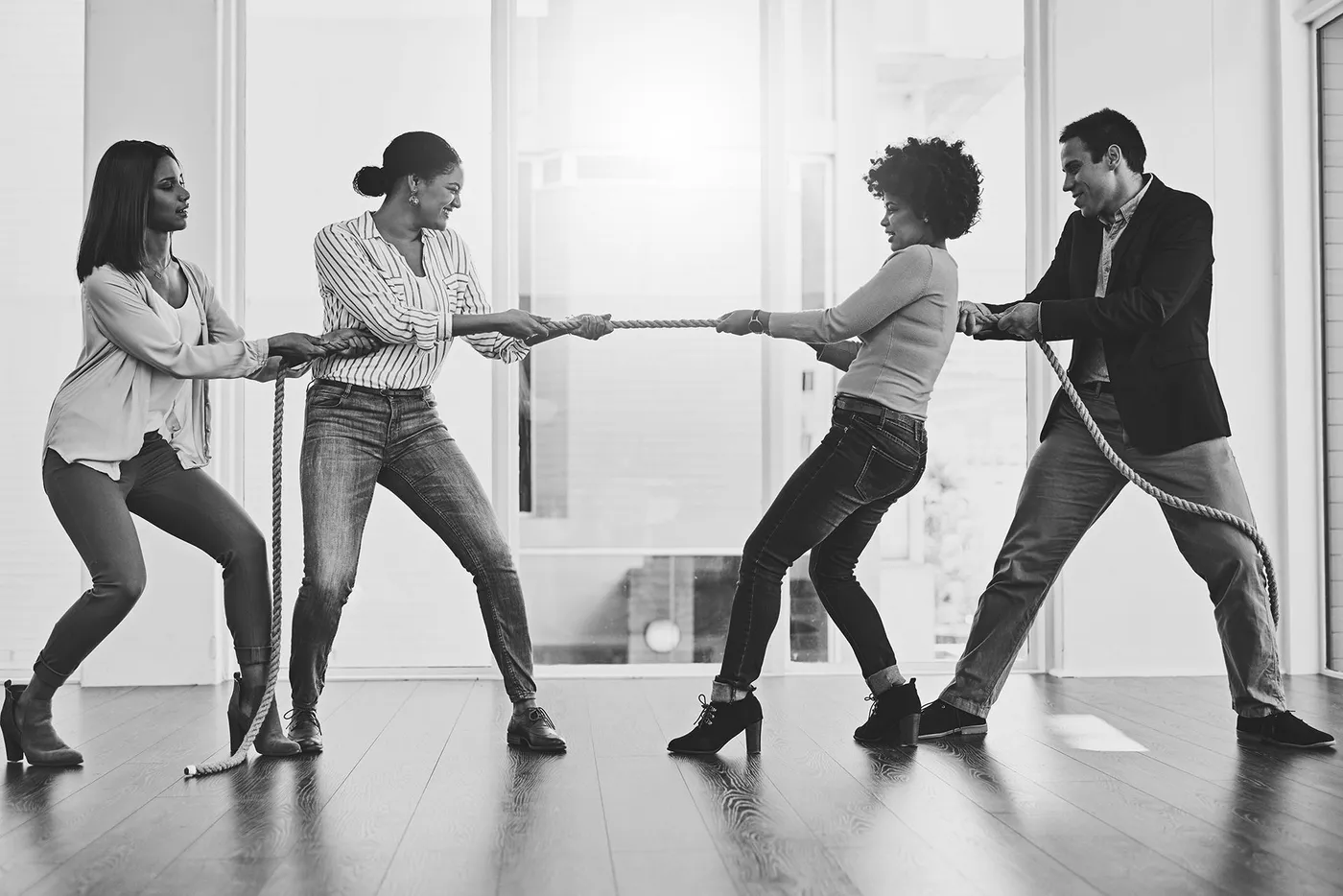 Four colleagues playing tug of war with a rope in a bright modern office space